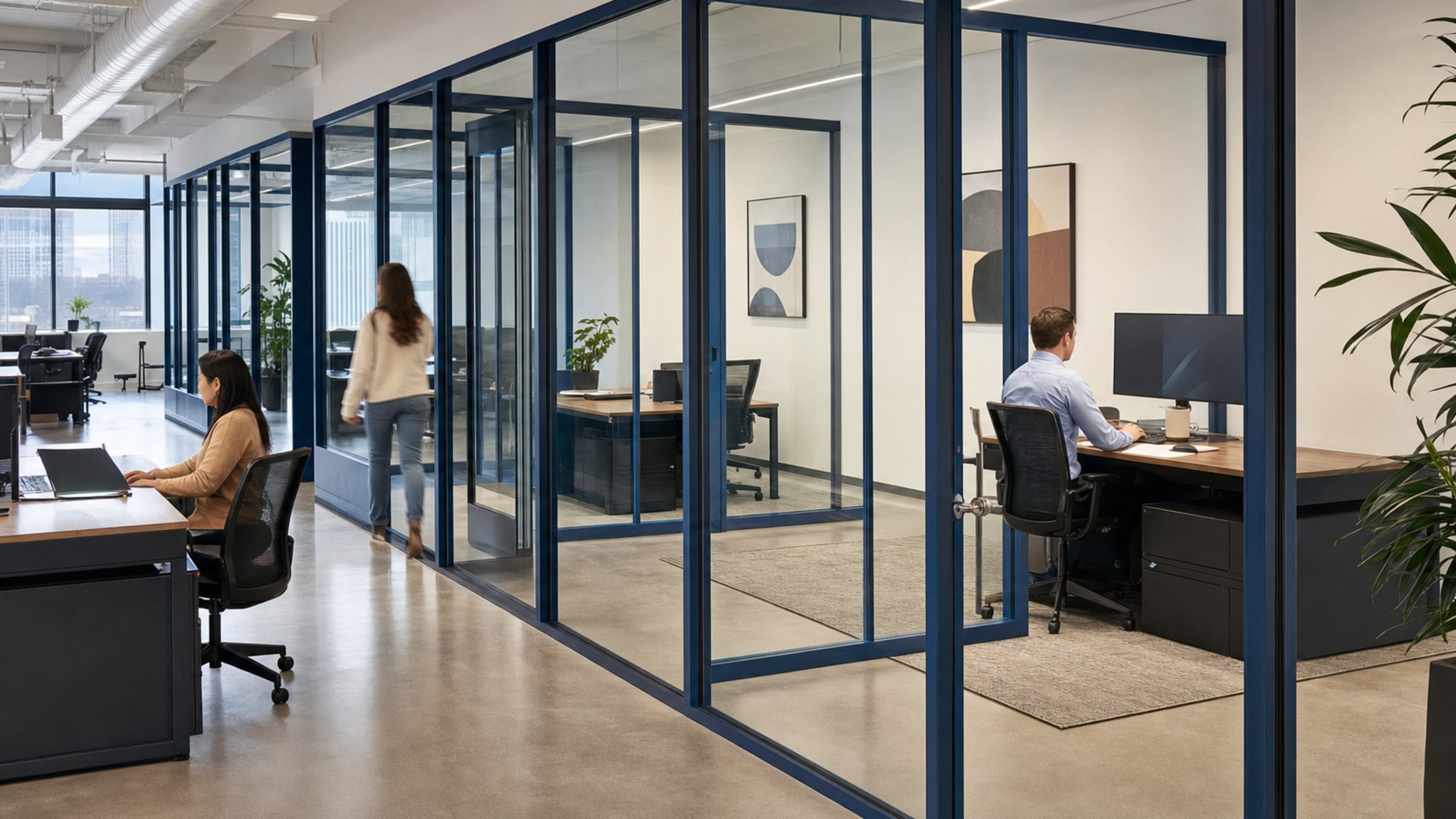 Interior office area with blue-framed frameless glass wall partitions and modern desks.